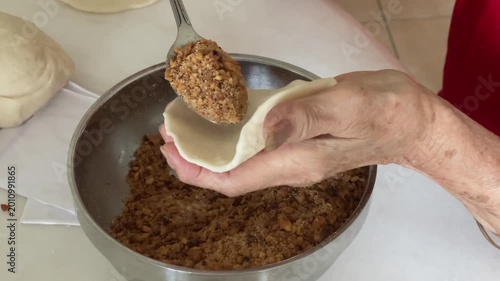 A slow motion shot shows a spoon pouring a generous amount of crushed peanut filling onto a round piece of dough to prepare handmade baozi.