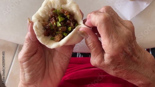 A close-up shot captures hands skillfully pleating the dough to complete a traditional handmade baozi filled with a savory mixture of minced meat and petai.
