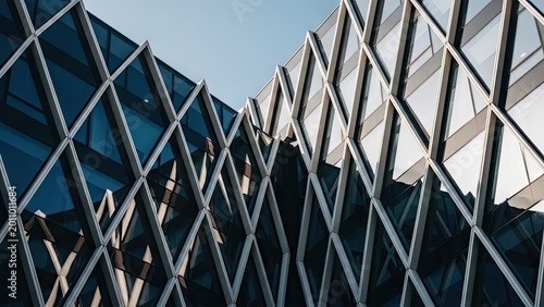 modern geometric glass building facade with reflective blue panels under clear sky