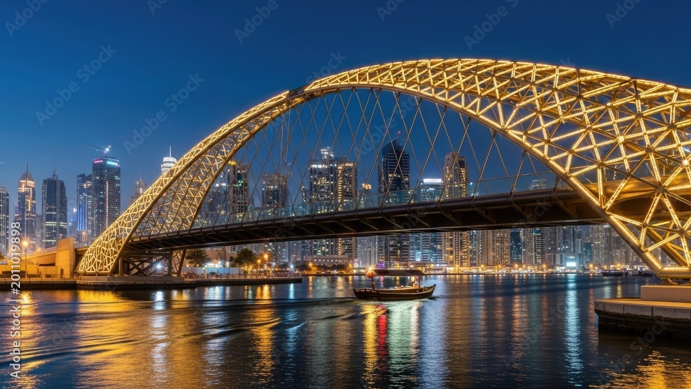 Fototapeta premium modern illuminated bridge at dusk over urban waterway with skyline and boat night scene