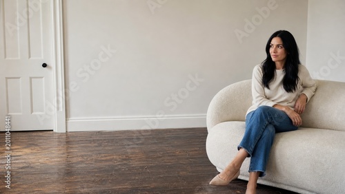 Young woman sitting on white curved sofa in bright minimalist empty room