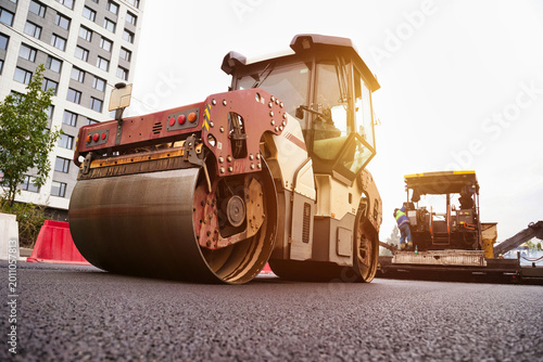 Foto Heavy machinery is actively paving asphalt on an urban roadway under bright sunlight