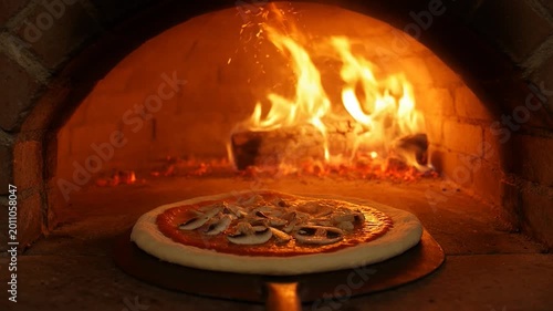 Uncooked pizza with mushrooms is placed in a hot wood-fired oven