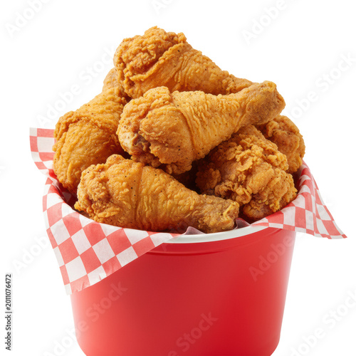 Crispy, golden-brown fried chicken (drumsticks and wings) with textured, spiced breading, stacked in a vibrant red takeaway bucket lined with checkered paper, isolated on white, intensely appetizing