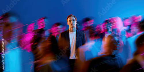 Young businessman standing still as colorful neon crowd rushes past in dynamic glitch motion