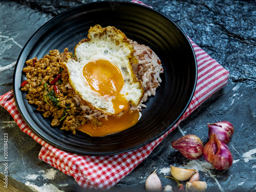 Stir fried minced pork basil chili steamed rice topped with fried egg served on black plate rustic background spicy savory traditional Thai cuisine appetizing meal