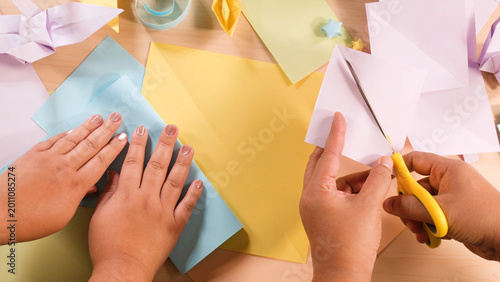 Foto Hands Folding Blue Paper and Cutting White Paper with Yellow Scissors