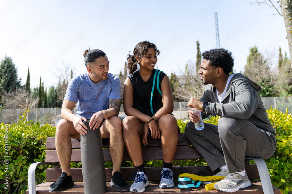 Naklejka premium Diverse group of friends sitting on a park bench, resting and talking after an outdoor fitness session