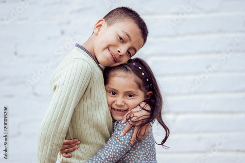 Brother and sister hugging each other in front of white wall