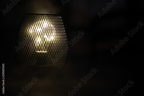 Tableau sur toile Dimly Lit Metal Wire Lamp with Soft Glowing Light in Dark Ambience