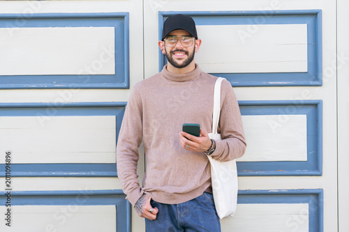 Smiling man holding smartphone standing against ornate wall