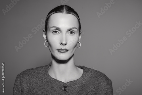 Cuadro en lienzo Portrait of a serious white woman in her thirties with light skin and slicked back hair wearing a textured jacket against a plain background