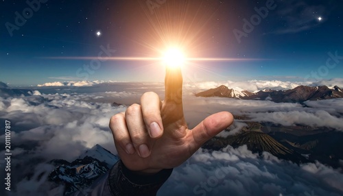 Finger touching bright light over mountain range and clouds against blue sky