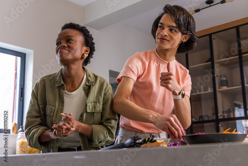 Diverse friends chopping, stirring and tasting food at kitchen counter with frying pan, utensils