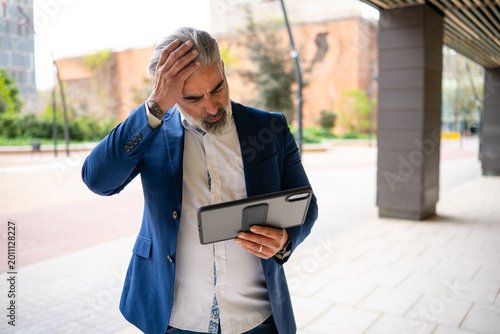 Stressed businessman receiving bad news on tablet outdoors