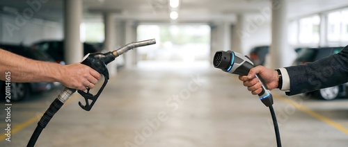 Comparison of gas pump nozzle and EV charging plug held in parking garage