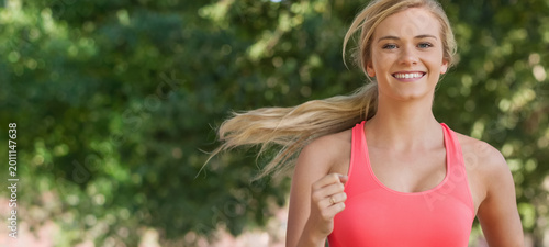 Obraz na płótnie Female jogging toward camera in park wearing coral pink athletic tank, hair tied