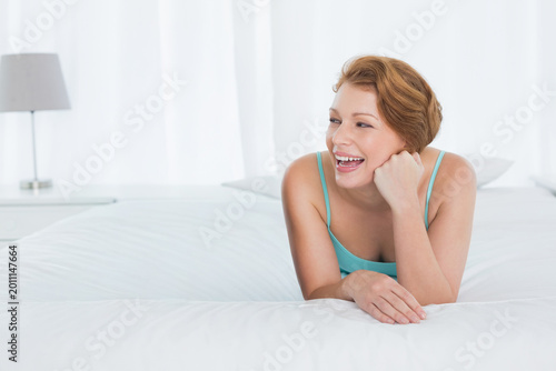 Foto Female reclining on large white bed in bright bedroom, wearing teal camisole, co
