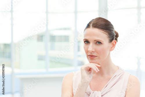 Woman holding chin, wearing pale blouse, gazing through grid windows in bright office, copy space Free Download Woman holding chin, wearing pale blouse, gazing through grid windows in bright office, copy space - GFXLoad