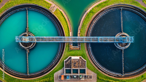 The view shows two large circular tanks at a water treatment facility with different colored water and a bridge connecting them across the center