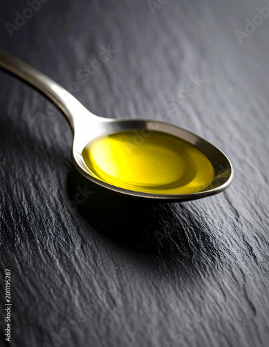 A spoon of olive oil on dark stone background