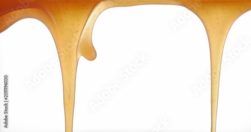 Close up macro of fresh homemade caramel sauce flowing and stretching on a white background. Smooth, glossy and sweet texture of soft caramel in motion. Dessert topping concept with rich golden color