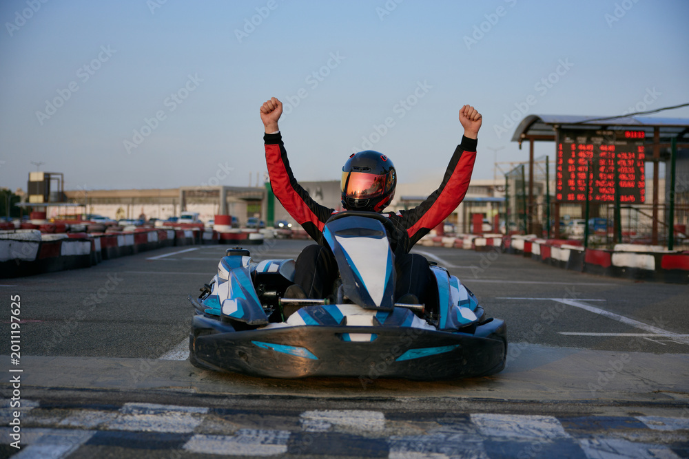 Fototapeta premium A go-kart racer celebrates a successful lap, raising hands in triumph on the track