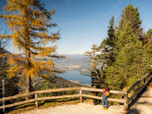 Woman hiker enjoying panoramic autumn mountain view over Lake Lavarone and valley, promoting travel and outdoor lifestyle in Lavarone, Trentino, Italy.
