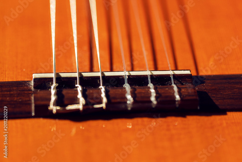 Foto Bridge of classical guitar with nylon strings stretched across a warm orange soundboard