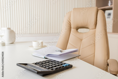 Beige leather chair, laptop and desk in office.Modern workplace.Stylish workplace with laptop, cup of coffee. elegant personal accessories in home decor.
