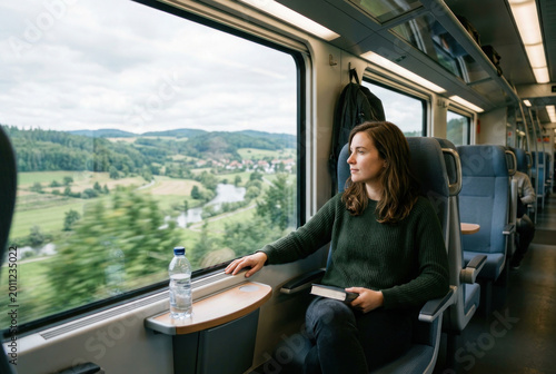 Young Woman Traveling by Train Through Scenic Countryside. Modern rail travel, sustainable transportation, relaxation, mobility, and scenic exploration concept.