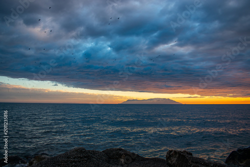 Dramatic sunset over the sea with dark clouds and island silhouette