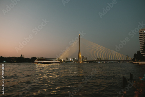 Dramatic twilight view of the iconic Rama VIII Bridge (Rama 8 Bridge) spanning the Chao Phraya River in Bangkok, Thailand. The striking asymmetrical cable-stayed bridge is beautifully illuminated, its