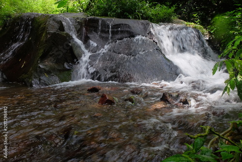 beautiful waterfall with trees and coral. water flows over dark, rugged stones, rocks creating staircase effect. The scene is serene natural landscape.