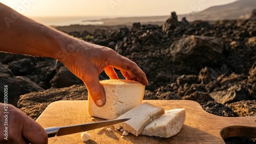 Close-up of Farmer's Hands Cutting Traditional Canarian Goat Cheese on a Volcanic Lava Field at Sunset.