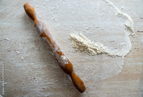 Classic timber baking tool lies diagonally across stone countertop scattered with fine wheat powder during professional pastry preparation in home kitchen
