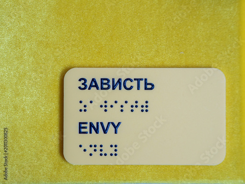 Fotografie Yellow plastic accessibility plate displays word envy in english and russian cyr