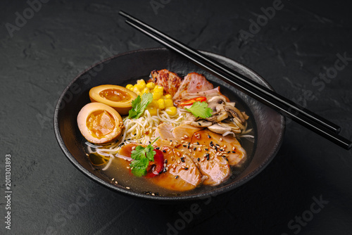 Warm bowl of ramen with toppings served in black bowl on dark surface