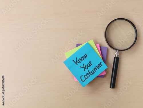 Know your customer text on adhesive note with magnifying glass on wooden background. Represents market research, consumer behavior analysis, target audience identification, and business strategy