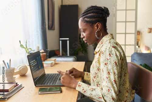 Foto Young African American woman checking smartphone beside laptop and passport, preparing for trip and managing travel booking