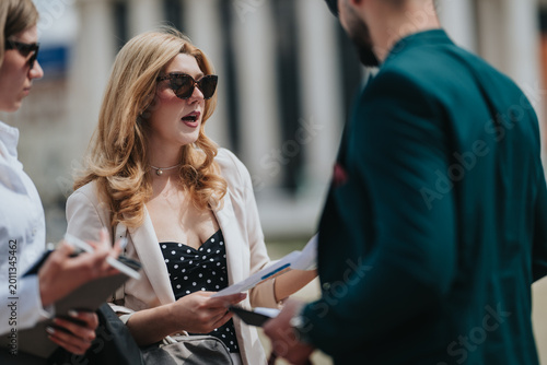 Business people review documents and talk outdoors. A small group of professionals discuss papers during an outdoor meeting.