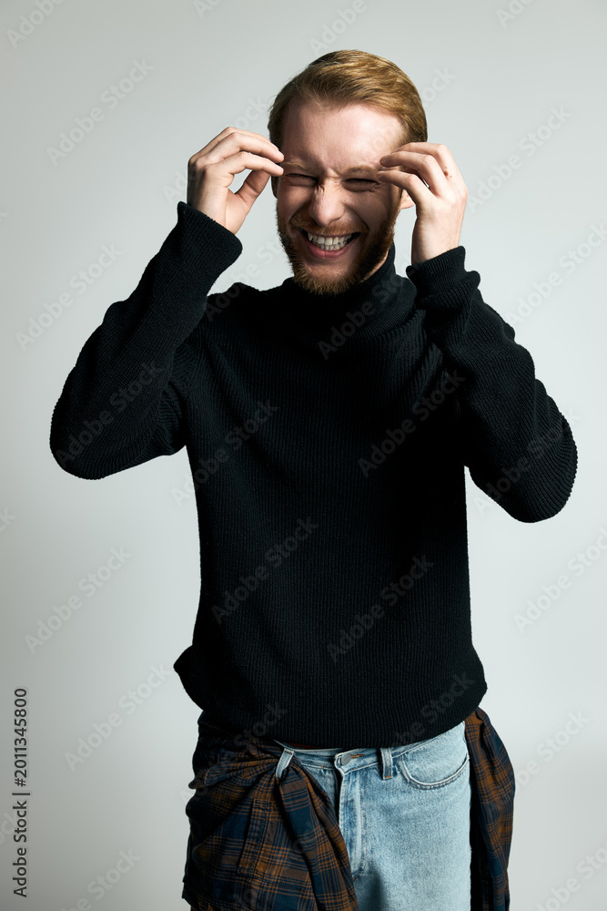 Fototapeta premium Stylish young man joyfully laughing against a simple backdrop.