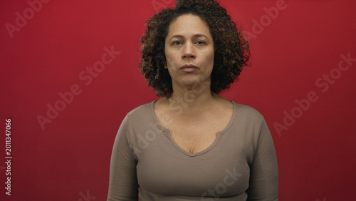 Fotografía Woman middle age hispanic with visible cleavage and subtle expression against red studio wall; contemplation
