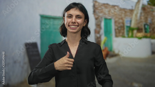 Bild auf Leinwand Young hispanic woman wearing black shirt and visible tattoos holding both thumbs up gesture in a street; confidence