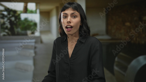 Картината върху платно Young hispanic woman wearing black shirt raises open palms by indoor spa pool in building; relaxation