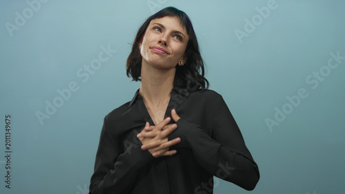 Canvastavla Young hispanic woman clutching chest in light blue studio, looking upward with gentle smile; serenity