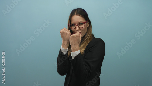 Bild auf Leinwand Woman in black blazer throwing a straight punch with visible fist toward camera in blue studio setting; determination