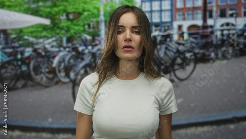 Cuadro en lienzo Young hispanic woman in white t-shirt flips middle fingers with bare hands on city street; anger defiance