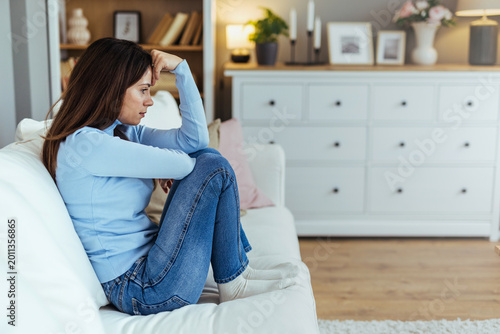 Pensive Young Woman Sitting on Couch at Home Feeling Anxious and Lonely in Living Room