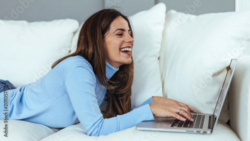 Smiling Young Woman Relaxing on Sofa Using Laptop at Home for Remote Work and Leisure